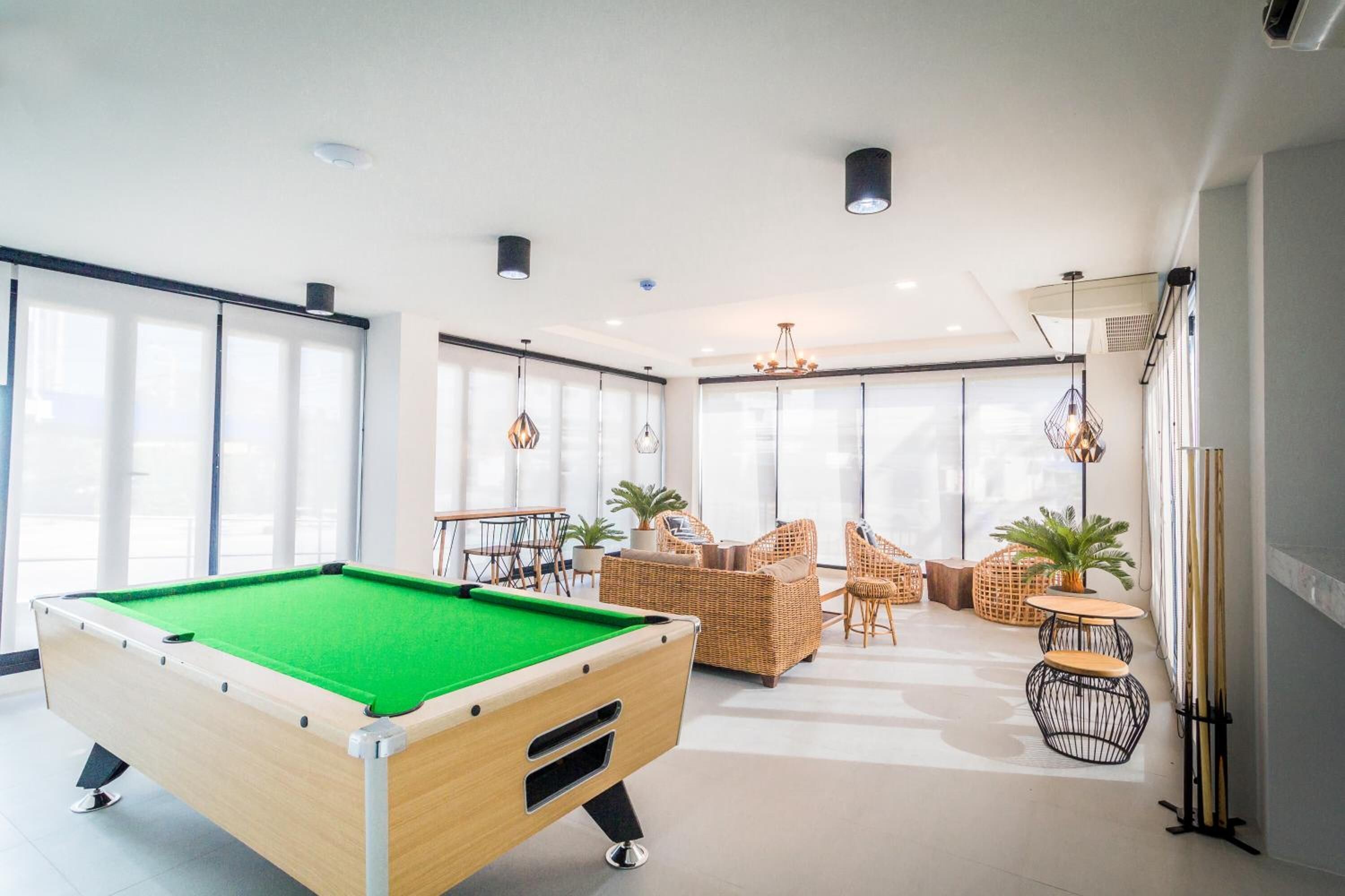 Una mesa de billar en una habitación luminosa con ventanas amplias, mobiliario de mimbre y un atril para billar.