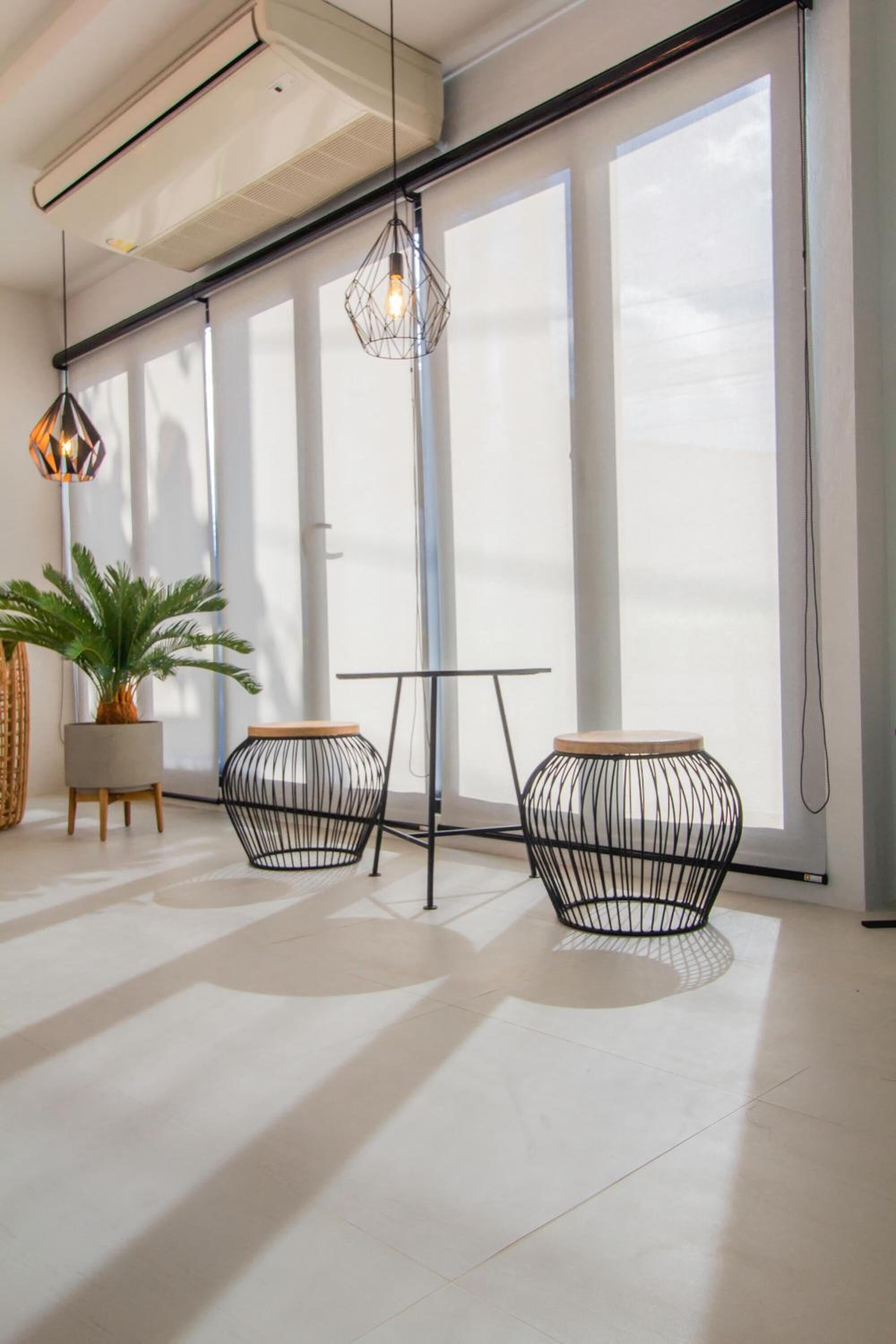 A modern interior with large windows, a ceiling air conditioner, and two wireframe tables with wooden tops.