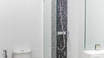 Uma casa de banho moderna com uma sanita branca, um chuveiro com parede de vidro e uma pia branca.