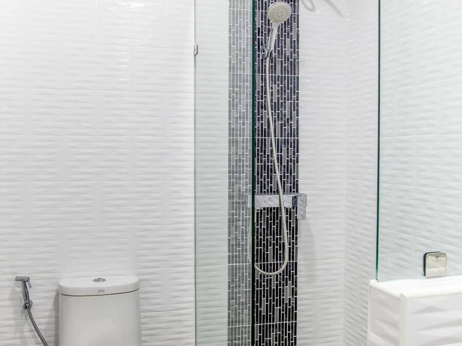 Uma casa de banho moderna com uma sanita branca, um chuveiro com parede de vidro e uma pia branca.