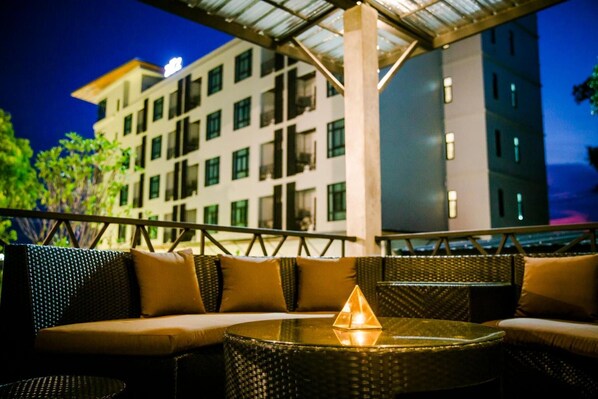 An outdoor seating area with wicker furniture and a glass table, overlooking a modern building with multiple windows. - Triple Z Hotel (Hua Hin)