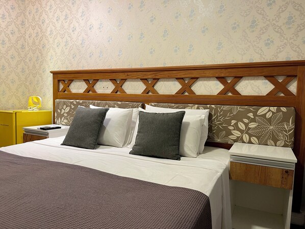 A neatly made bed with a wooden headboard, a bedside table with a lamp, and a yellow cabinet.