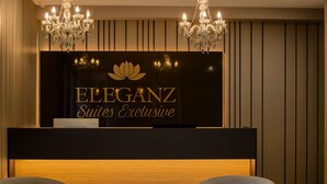A reception desk with a sign reading "ELEGANZ Suites Exclusive" and two chandeliers above it. - Eleganz Hostel & Suites (Gramado)