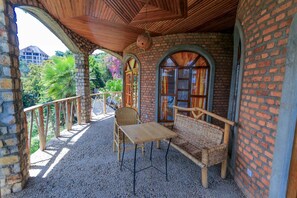 A covered outdoor seating area with a table and chairs, brick walls, and a view of greenery. - The Palm Beach Resort (Nyayumba)