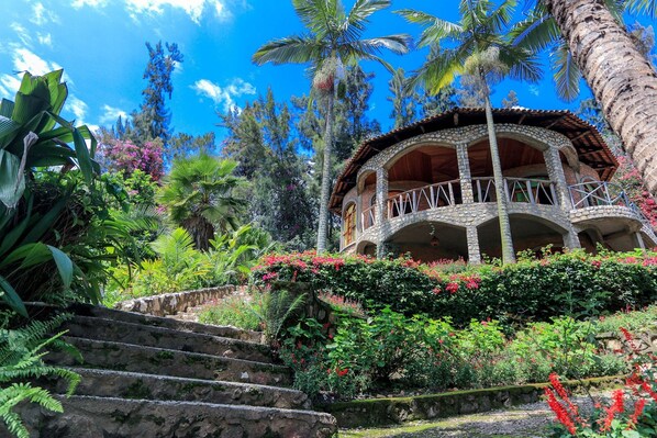 A stone building with a balcony, surrounded by lush greenery and palm trees. - The Palm Beach Resort (Nyayumba)