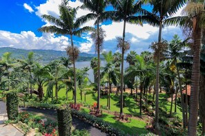 Un jardín tropical con palmeras, un sendero y vistas a un lago y montañas.