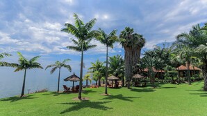 A tropical resort with palm trees, a beach, and thatched-roof huts. - The Palm Beach Resort (Nyayumba)
