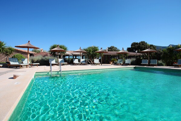 Een buitenzwembad, parasols bij het zwembad en ligstoelen