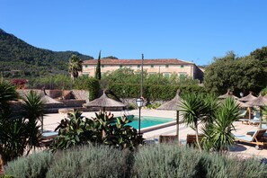 A resort with a swimming pool, lounge chairs, and thatched umbrellas. - Ca's Garriguer Agroturismo (Valldemossa)