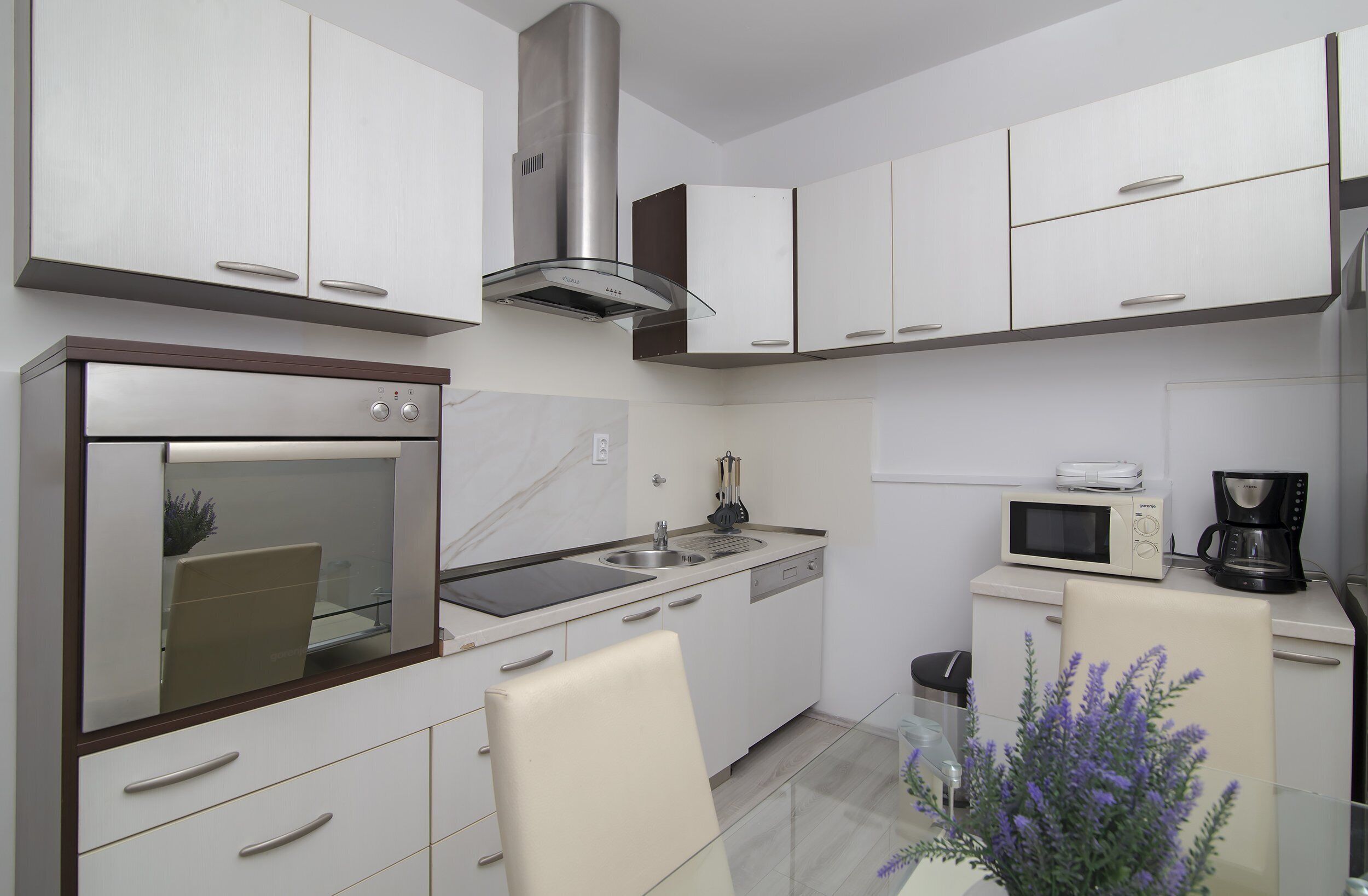 A modern kitchen with white cabinets, stainless steel appliances, and a glass dining table.