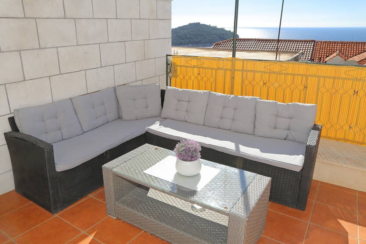 A balcony with a grey sofa, a glass coffee table, and a potted plant.