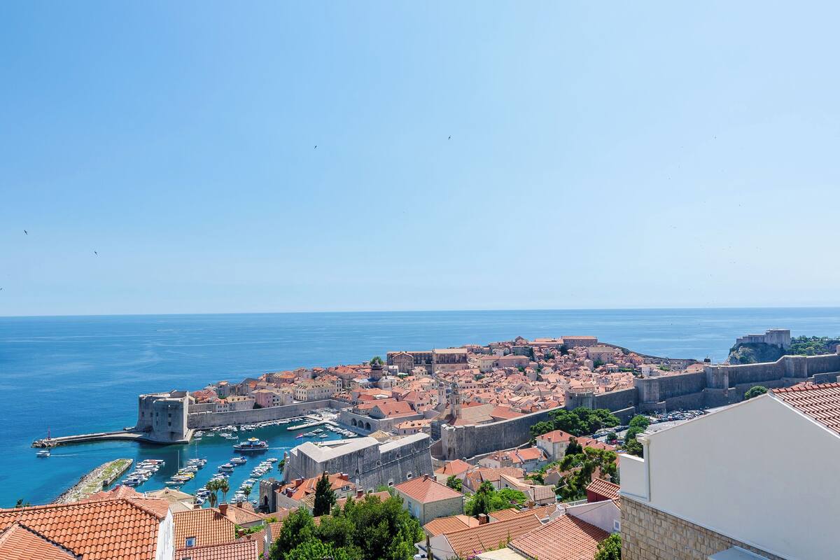 A coastal city with historic architecture, a harbor with boats, and a clear blue sky.