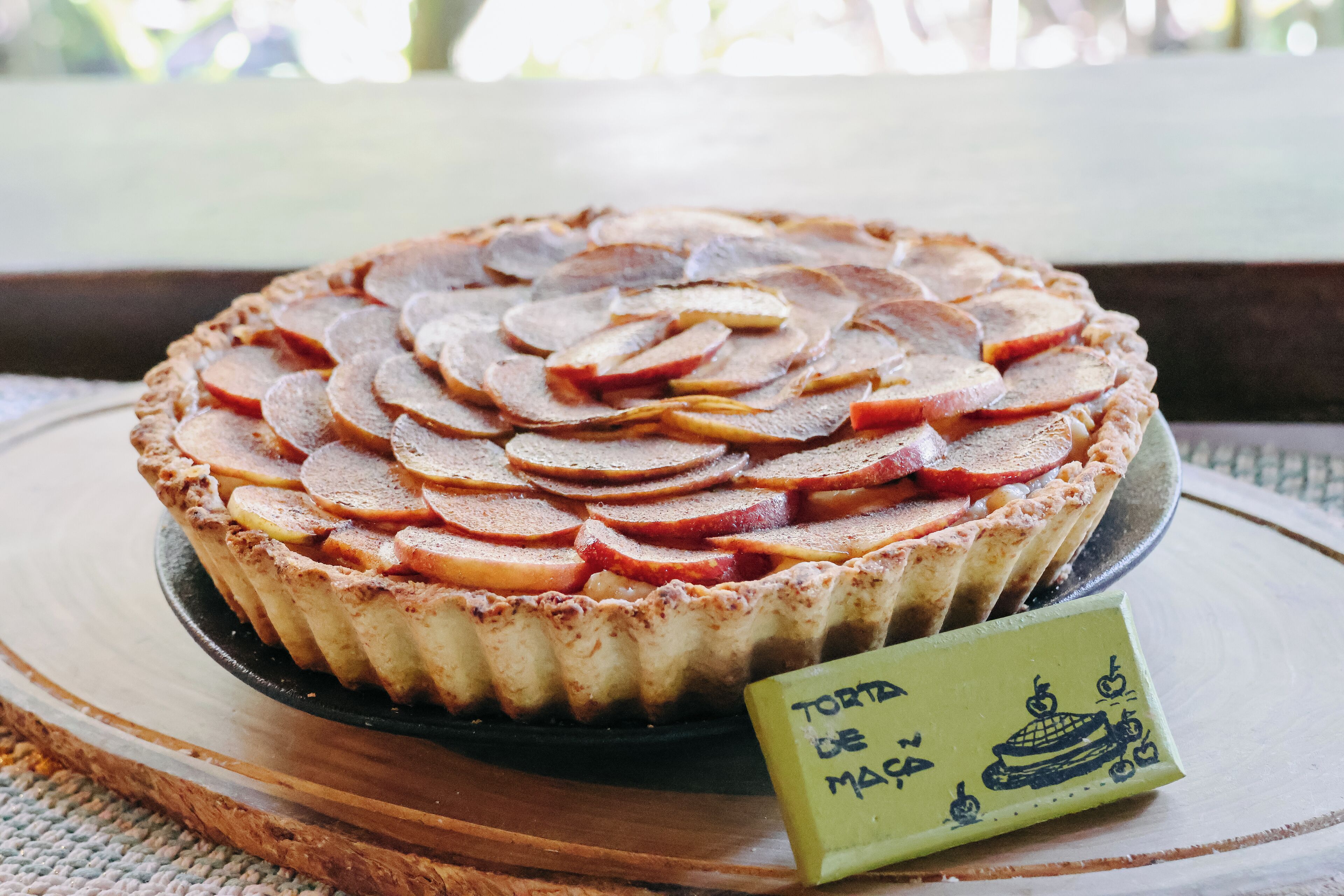 Ein Kuchen mit Apfelscheiben, auf einer Holzplatte serviert, neben der ein Schild steht.