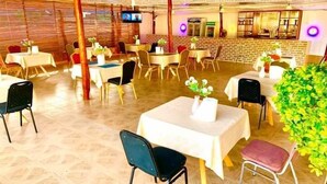 A restaurant with multiple tables and chairs, a television screen, and a brick wall. - Sundowner Lodge (Tamale)