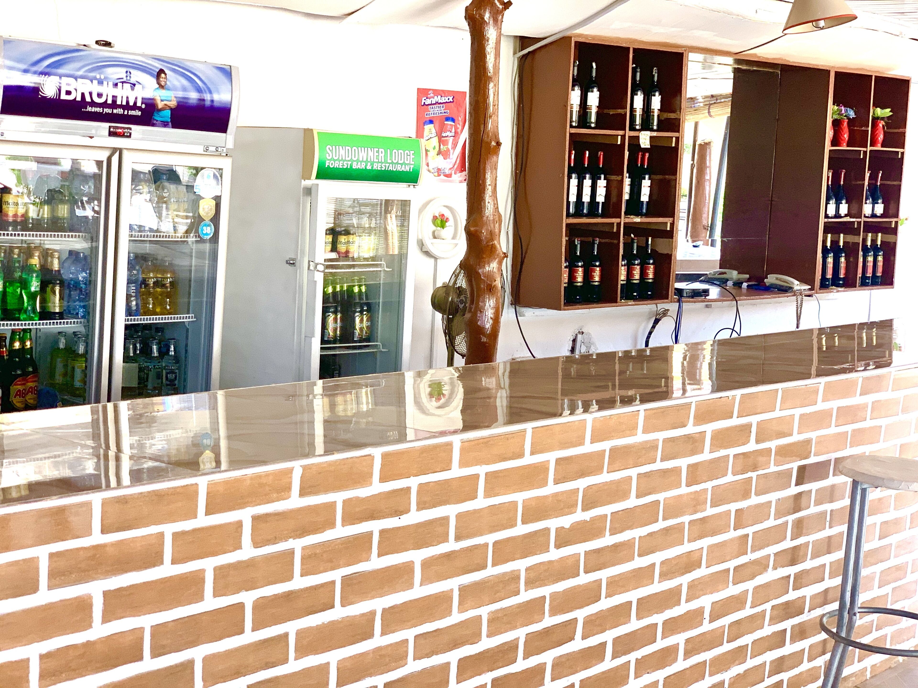 Una zona de bar con mostrador de ladrillo, un refrigerador lleno de bebidas y una estantería para vinos.