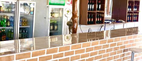 Una zona de bar con mostrador de ladrillo, un refrigerador lleno de bebidas y una estantería para vinos.