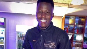 A person standing in a modern indoor setting with a brick wall and a counter. - Sundowner Lodge (Tamale)
