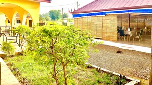 A courtyard with a dining area, covered seating, and a small tree. - Sundowner Lodge (Tamale)