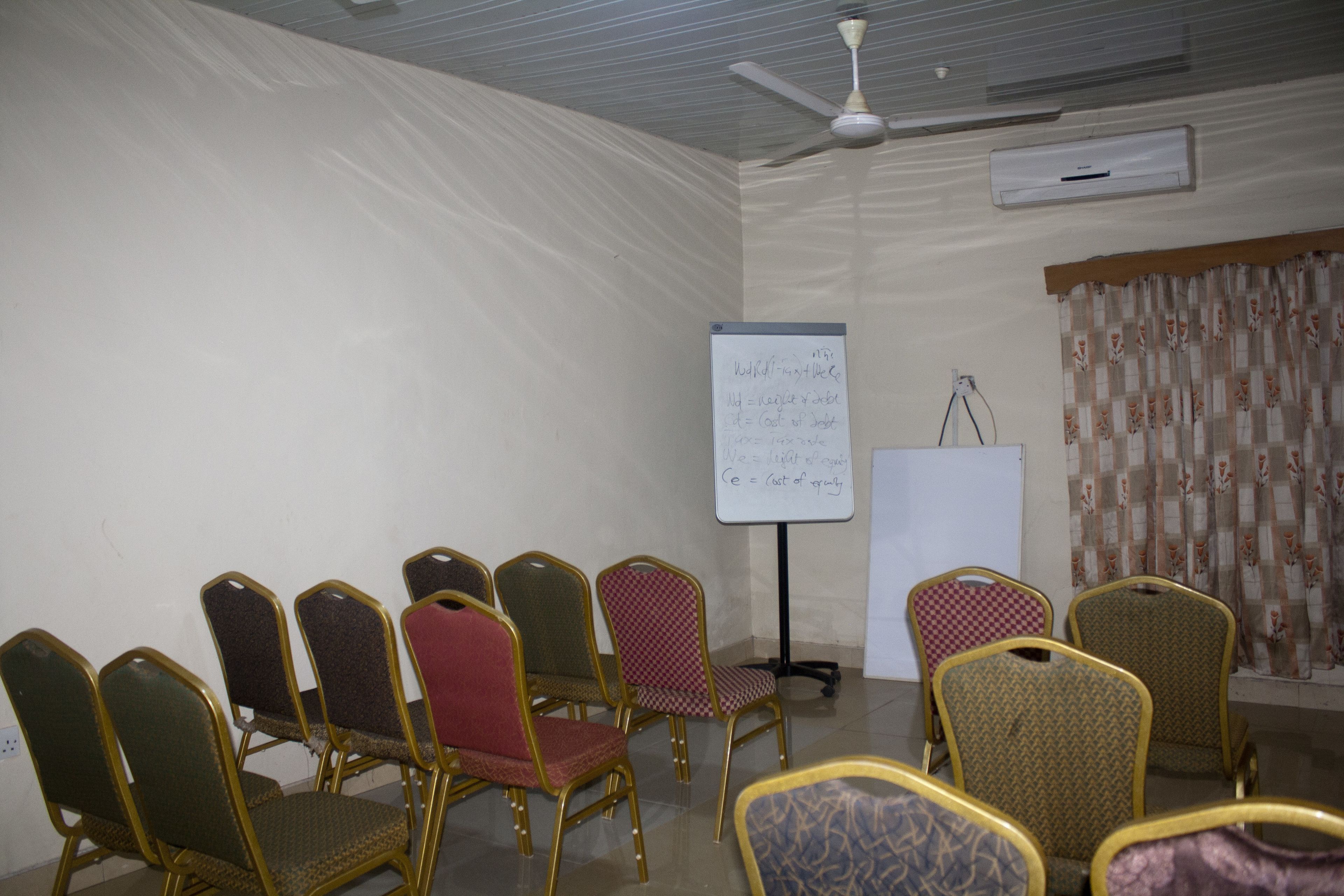 Ein Konferenzraum mit einer Whiteboard, einem Deckenventilator und mehreren Stühlen.