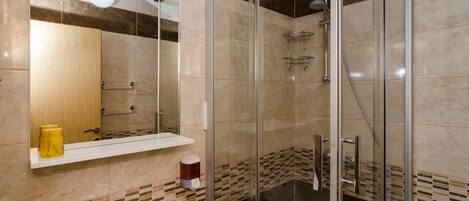 Un baño moderno con ducha envuelta en vidrio, un lavamanos con espejo y un estante con artículos de aseo.