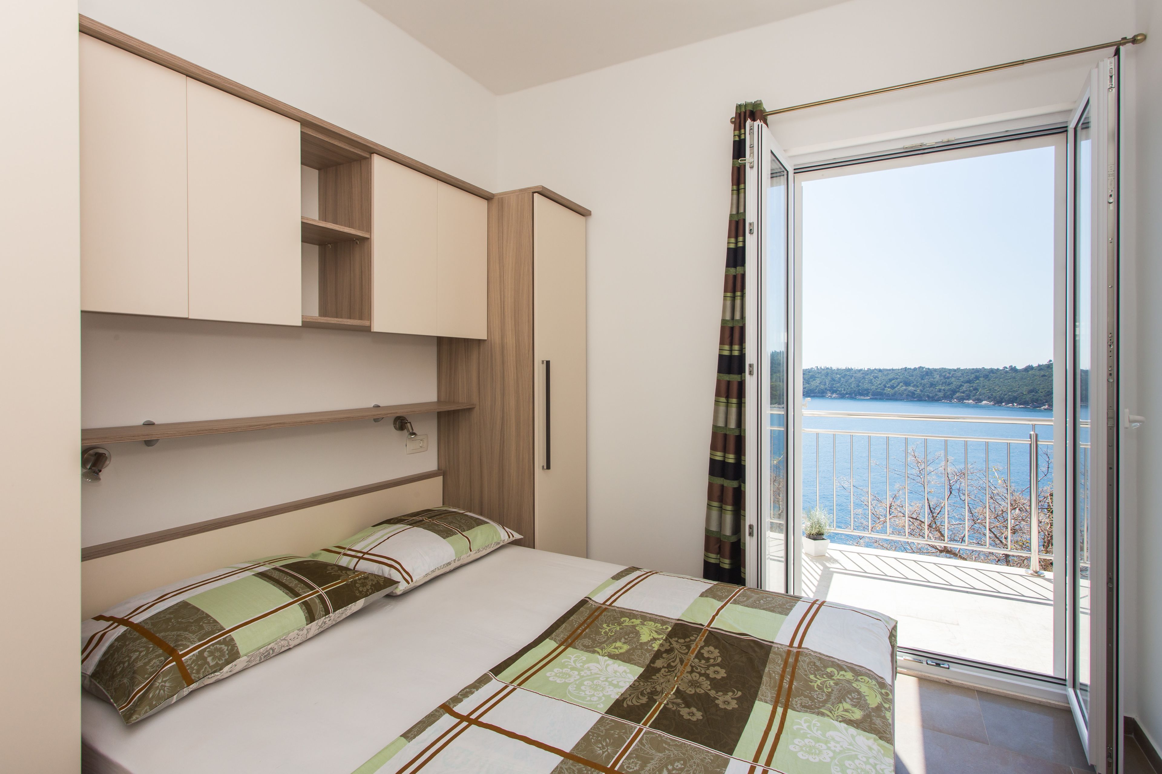 A bedroom with a bed, a built-in wardrobe, and a balcony with a view of the water.