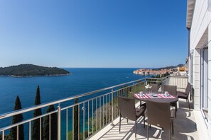 A balcony with wicker furniture, a table with a striped tablecloth, and a view of the sea and a distant island. - Apartments Villa Ari (Dubrovnik)