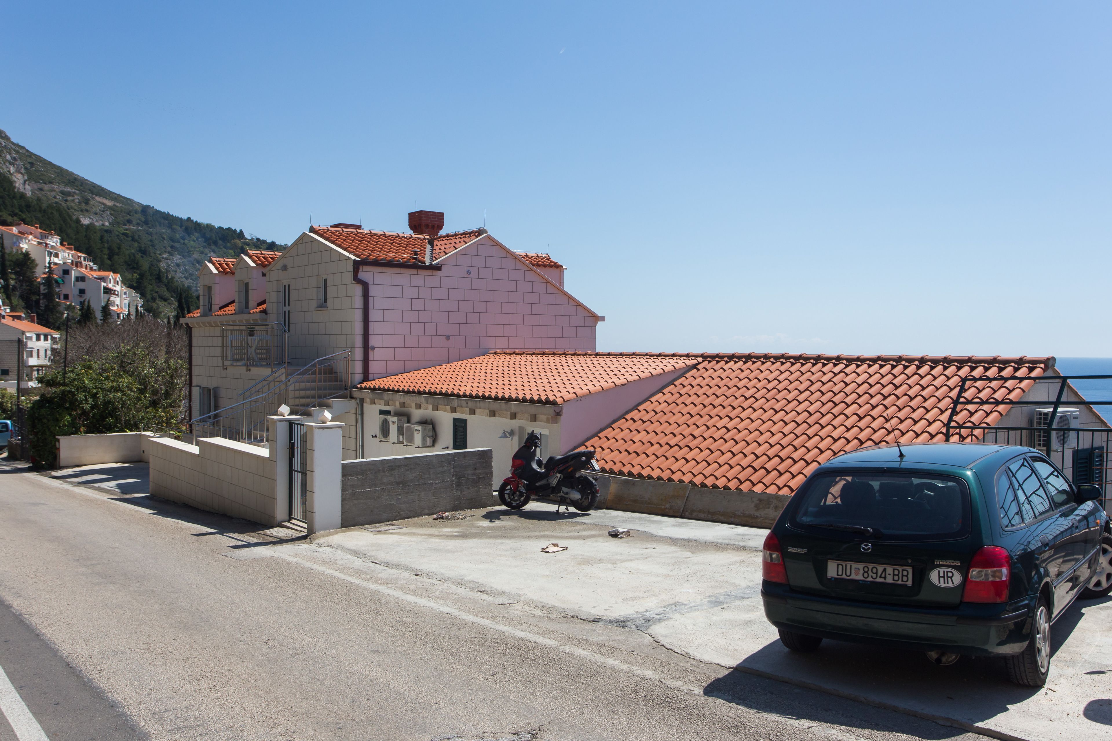 A residential area with a red-tiled roof house, a parked motorcycle, and a car on a paved road.
