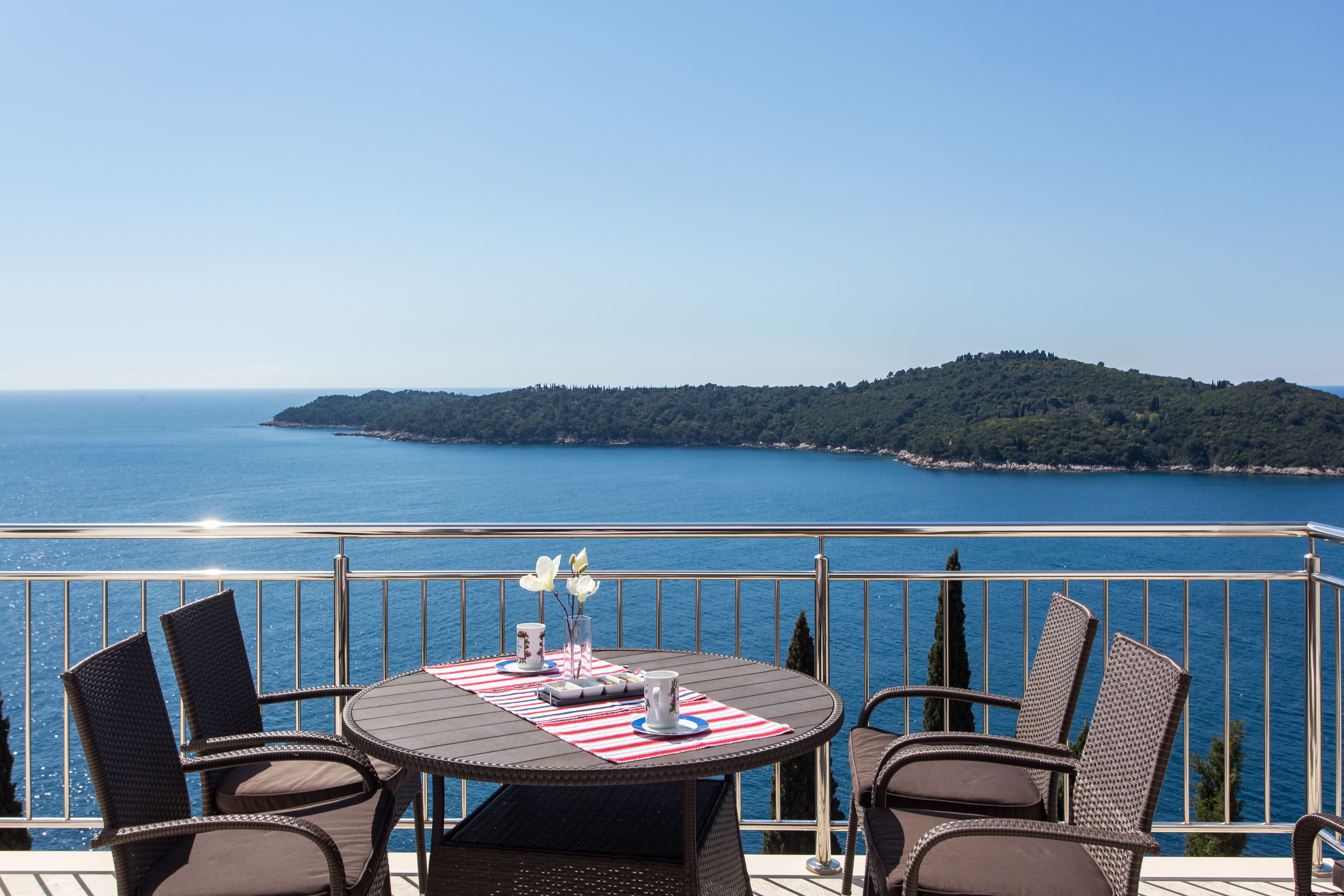 A balcony with a table and chairs overlooking a body of water and a distant island.
