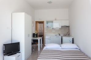 Habitación de hotel compacta con cama, televisor, escritorio y kitchenette.