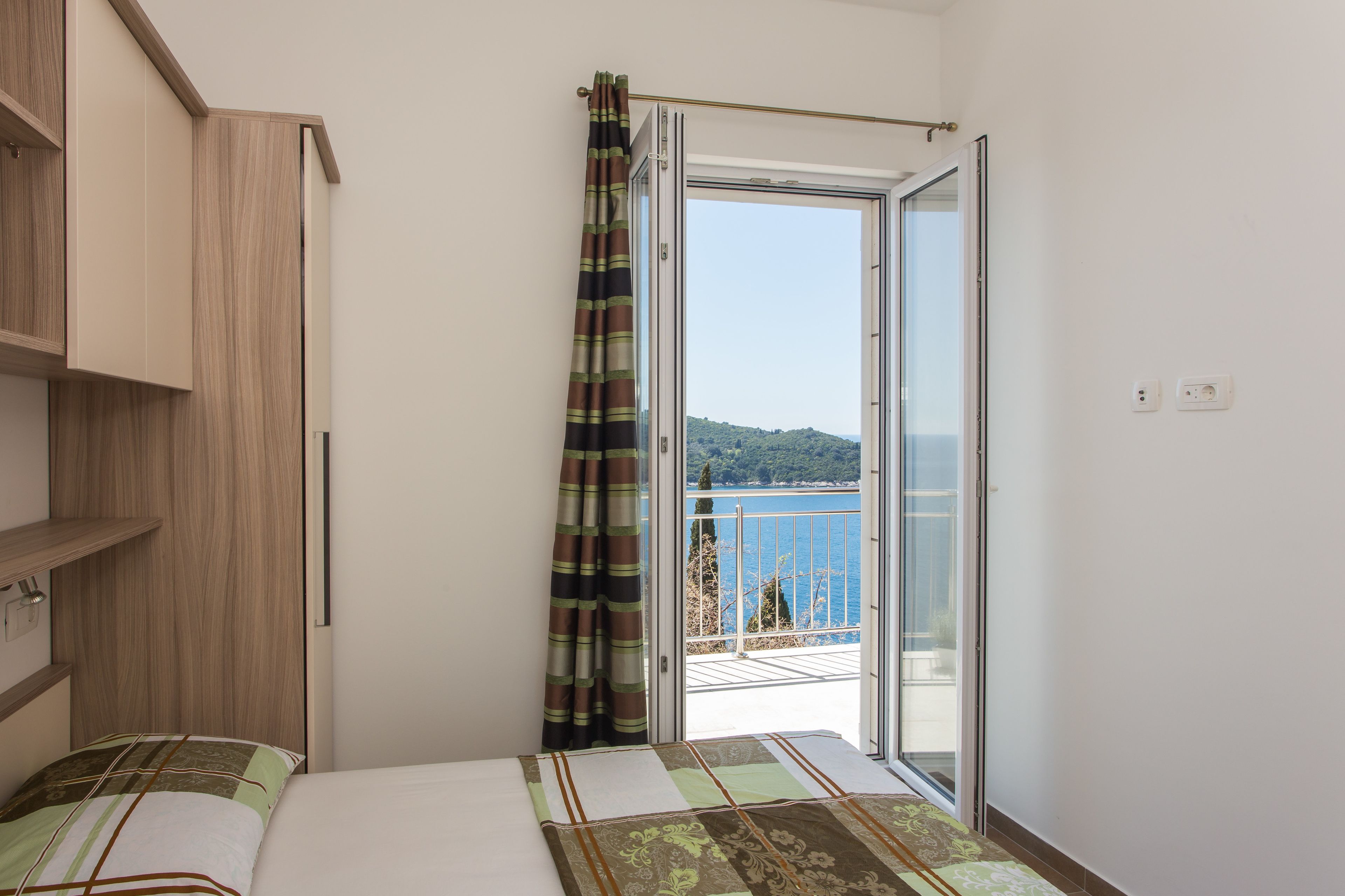 A bedroom with a bed, a wardrobe, and a balcony with a view of the sea.
