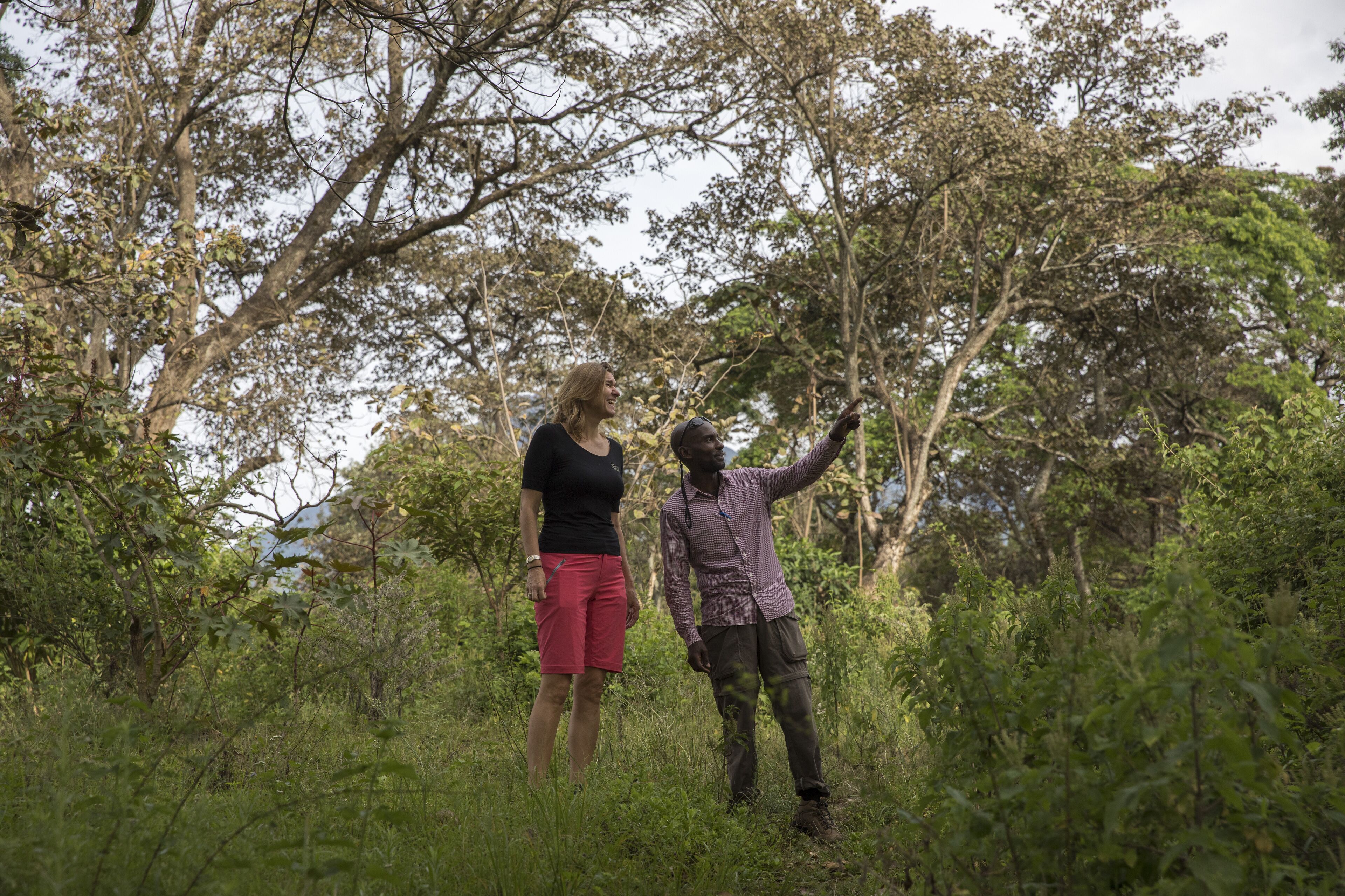 Two people standing in a natural setting with trees and greenery.