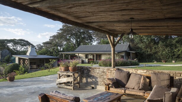 An outdoor patio area with wooden furniture, a stone wall, and potted plants. - Arusha Villa (Arusha)