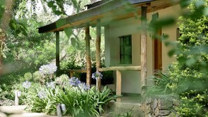 A rustic house with a wooden porch, surrounded by lush greenery and flowering plants. - Arusha Villa (Arusha)