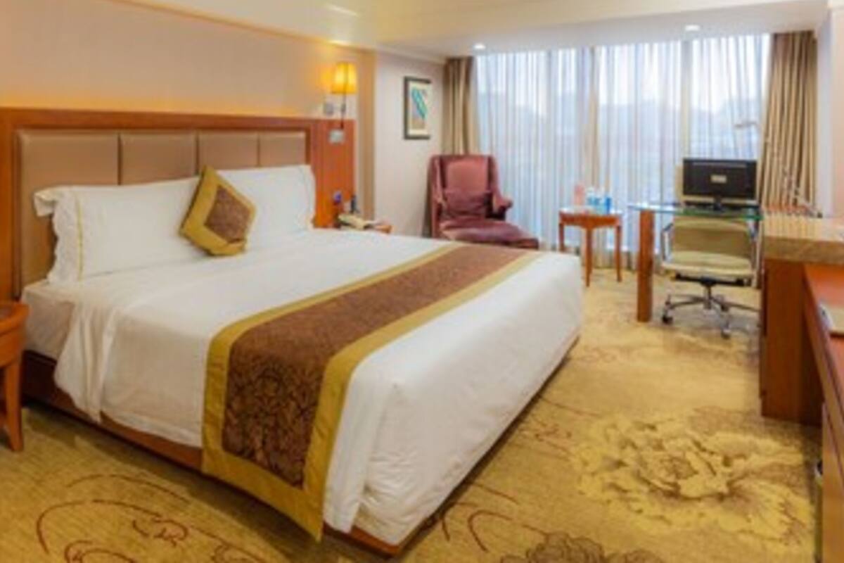 Una habitación de hotel con una cama grande, un escritorio con computadora, una silla y una ventana con cortinas.
