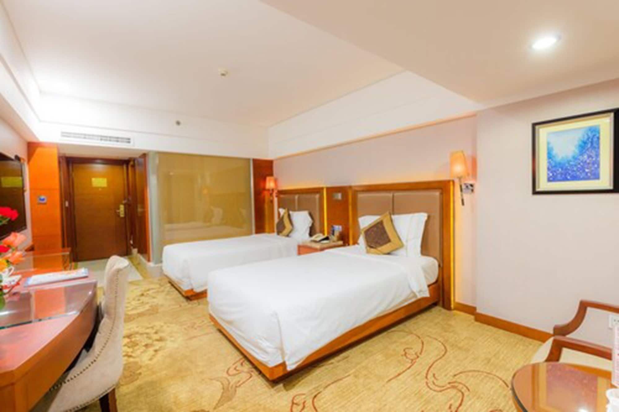 Habitación de hotel con dos camas individuales, un escritorio con silla, una mesita y un cuadro enmarcado en la pared.