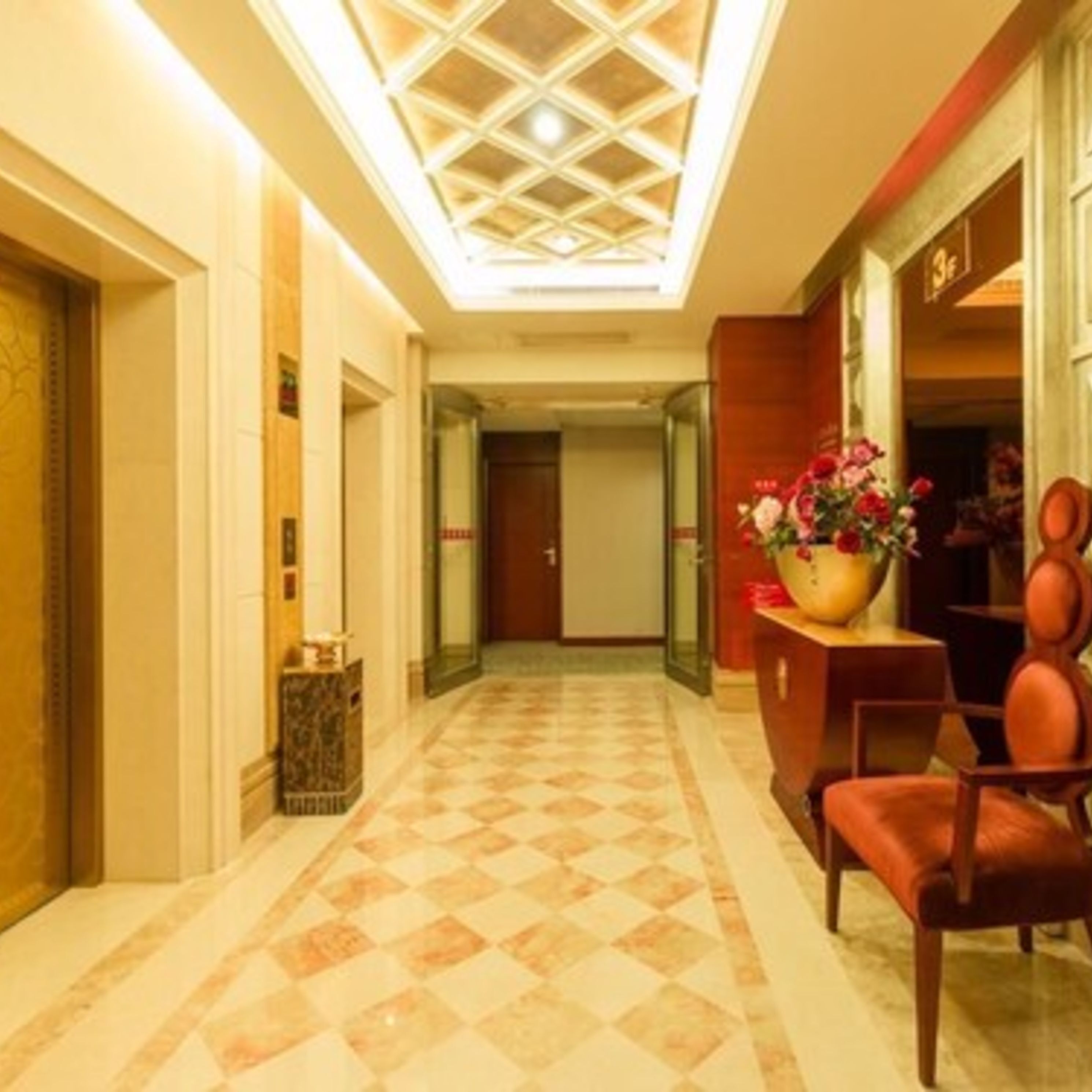 A hotel lobby with a checkered floor, a reception desk with a vase of flowers, and a wooden chair.