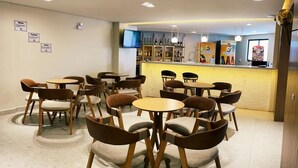 Een modern café met ronde tafels en bruine stoelen, een bar met flessen en een televisiescherm.