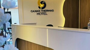 Een modern ontworpen receptiebalie bij Hotel Caxias Thermas, met een logo en een houten accentpaneel.