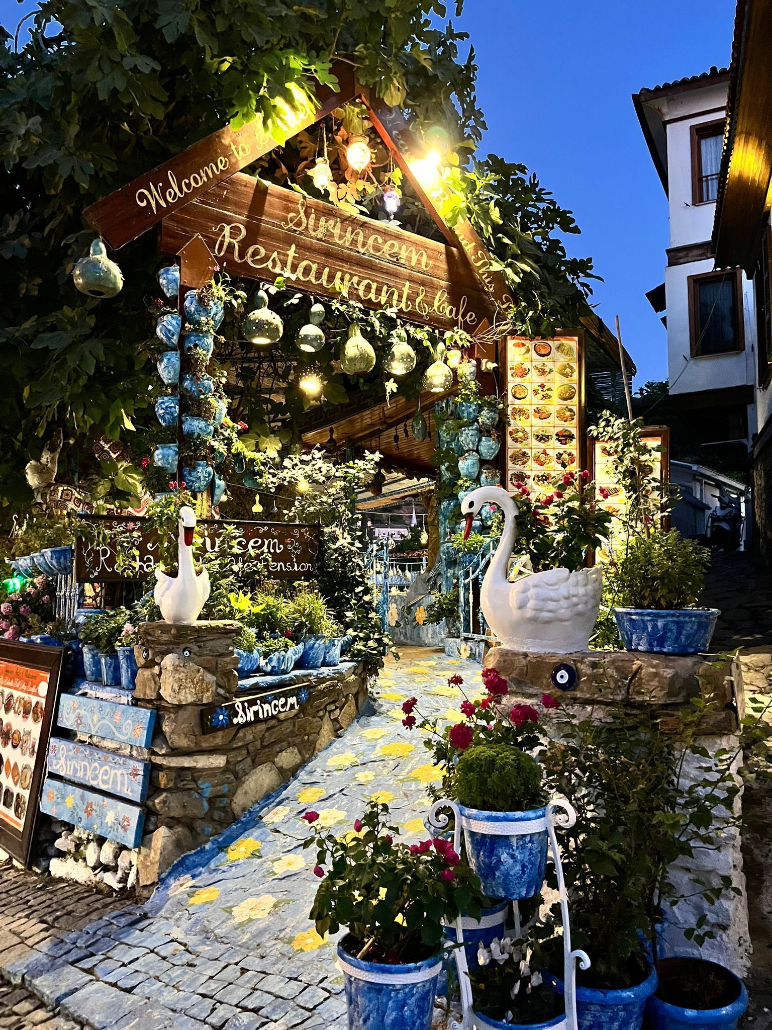 Entrada de un restaurante con un letrero acogedor, luces decorativas y una estatua de cisne.