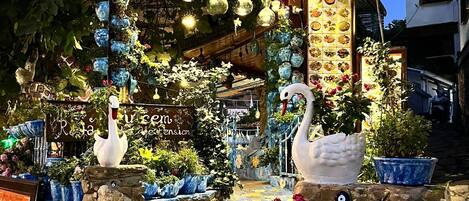 Entrada de un restaurante con un letrero acogedor, luces decorativas y una estatua de cisne.