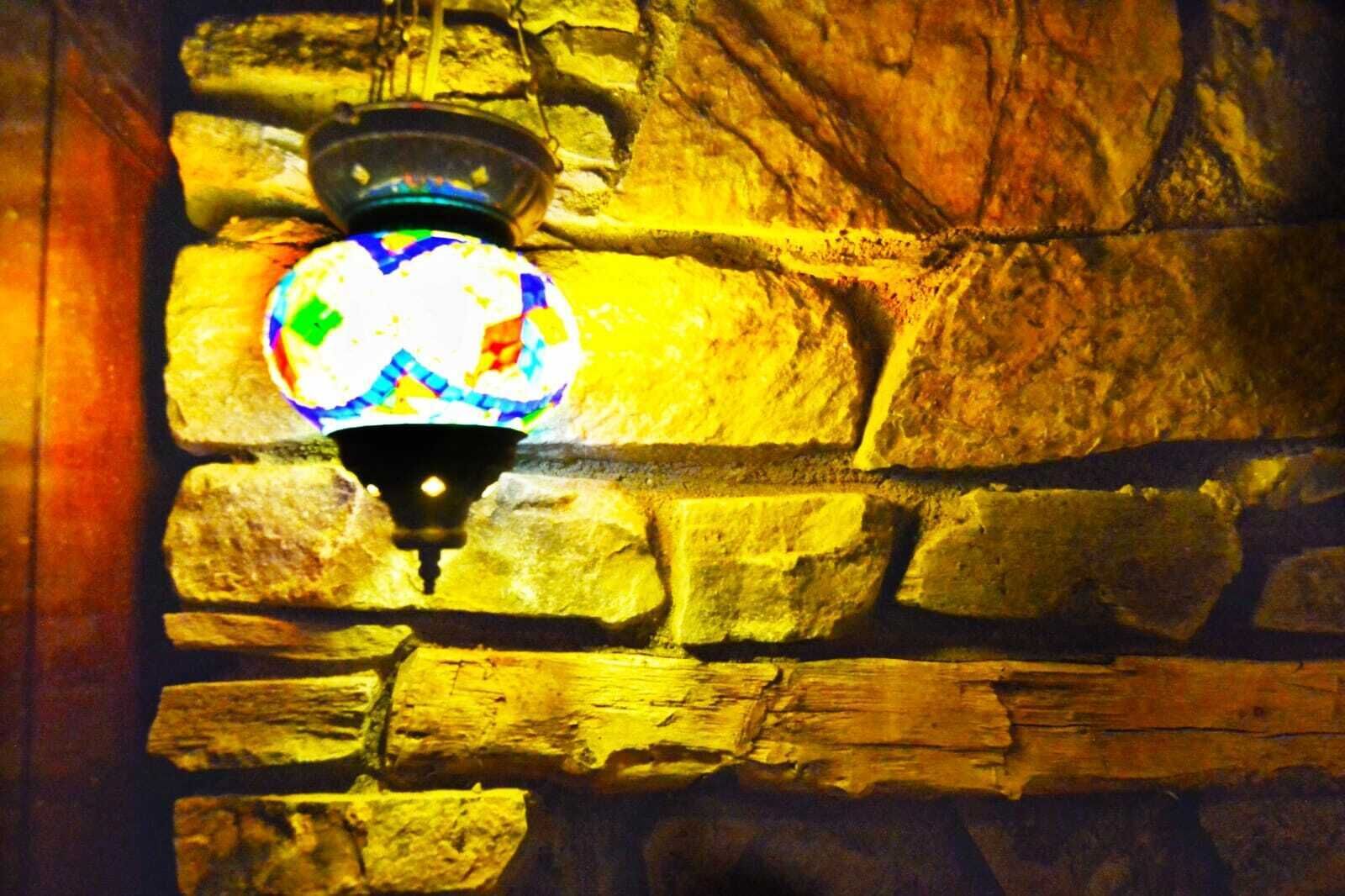 A mosaic lamp against a stone wall.