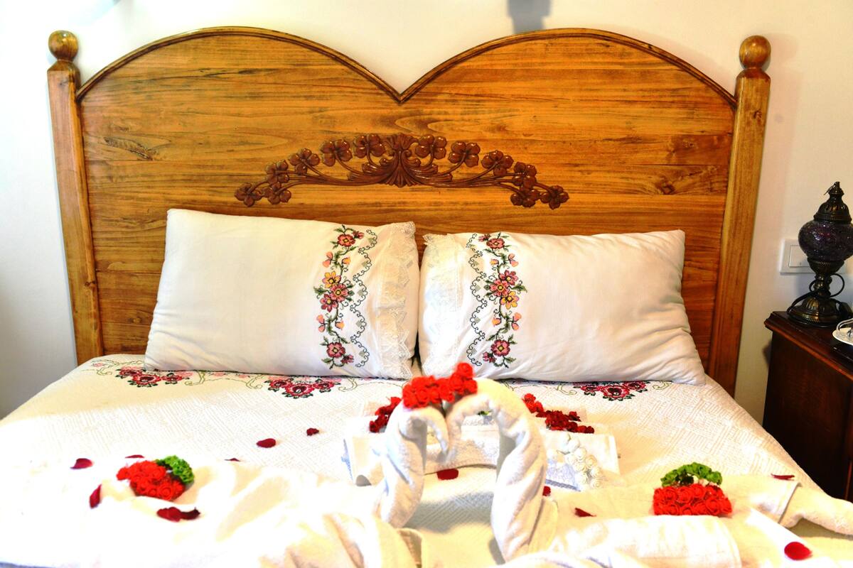 A wooden bed with floral embroidery, white pillows, and red roses arranged on the bed.