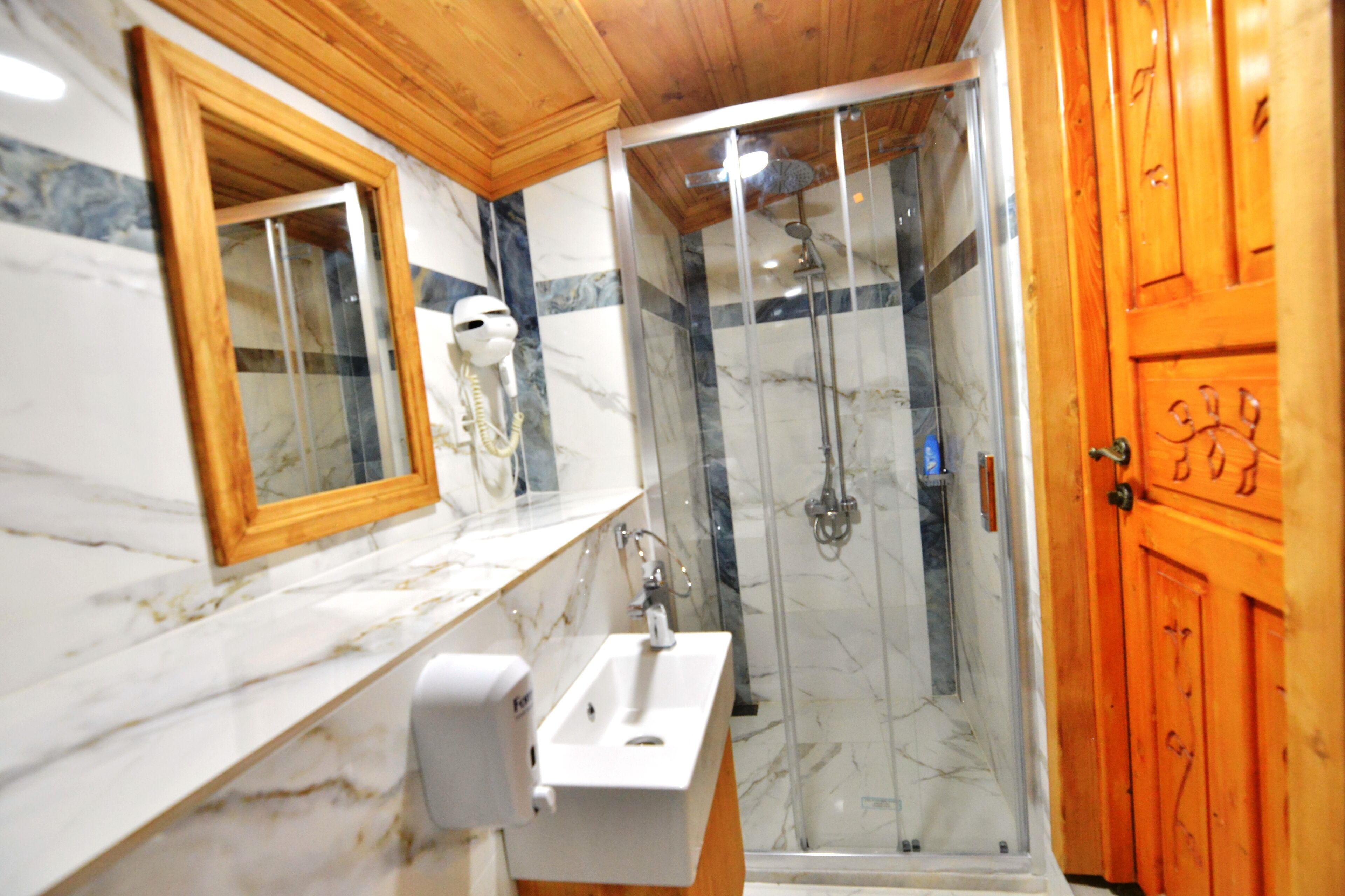 A bathroom with a marble countertop, a sink, a mirror, and a shower enclosure.