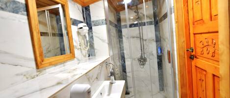 A bathroom with a marble countertop, a sink, a mirror, and a shower enclosure.
