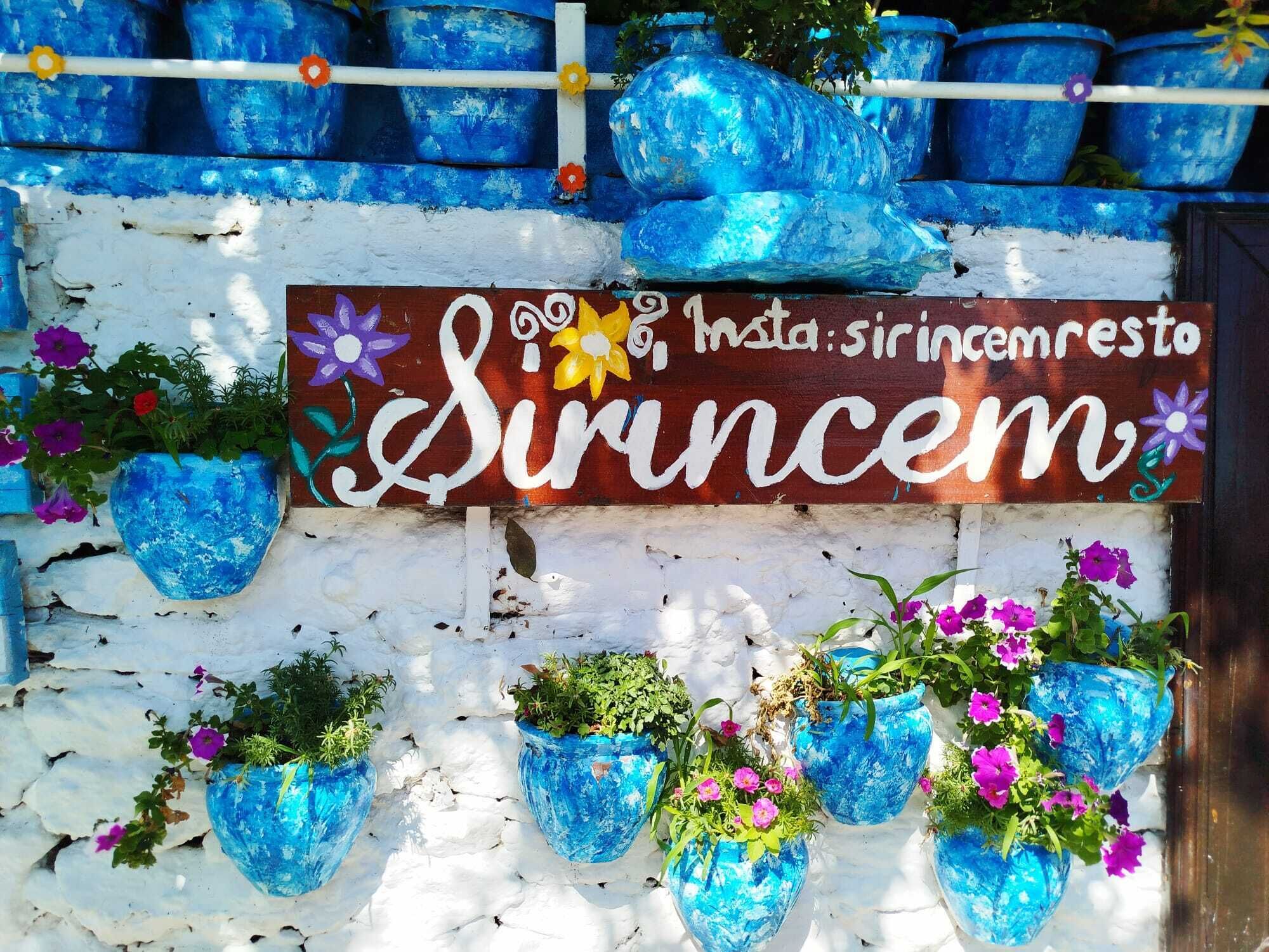 A wall with a sign reading "Sincem" and several blue hanging planters with flowers.