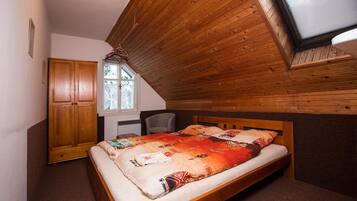 A bedroom with a sloped ceiling, a bed with a patterned blanket, a wooden wardrobe, and a window with a view of trees.