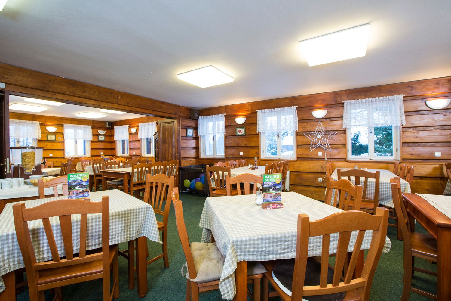 A cozy cabin-style dining area with wooden walls, checkered tablecloths, and multiple dining tables and chairs.