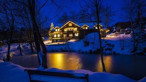 A snow-covered bench in front of a lit-up house by a frozen lake at night. - Chata Pod Lipami (Rokytnice nad Jizerou)