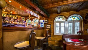 A bar area with wooden walls, a bar counter with liquor bottles, two bar stools, and a wooden cabinet. - Chata Pod Lipami (Rokytnice nad Jizerou)