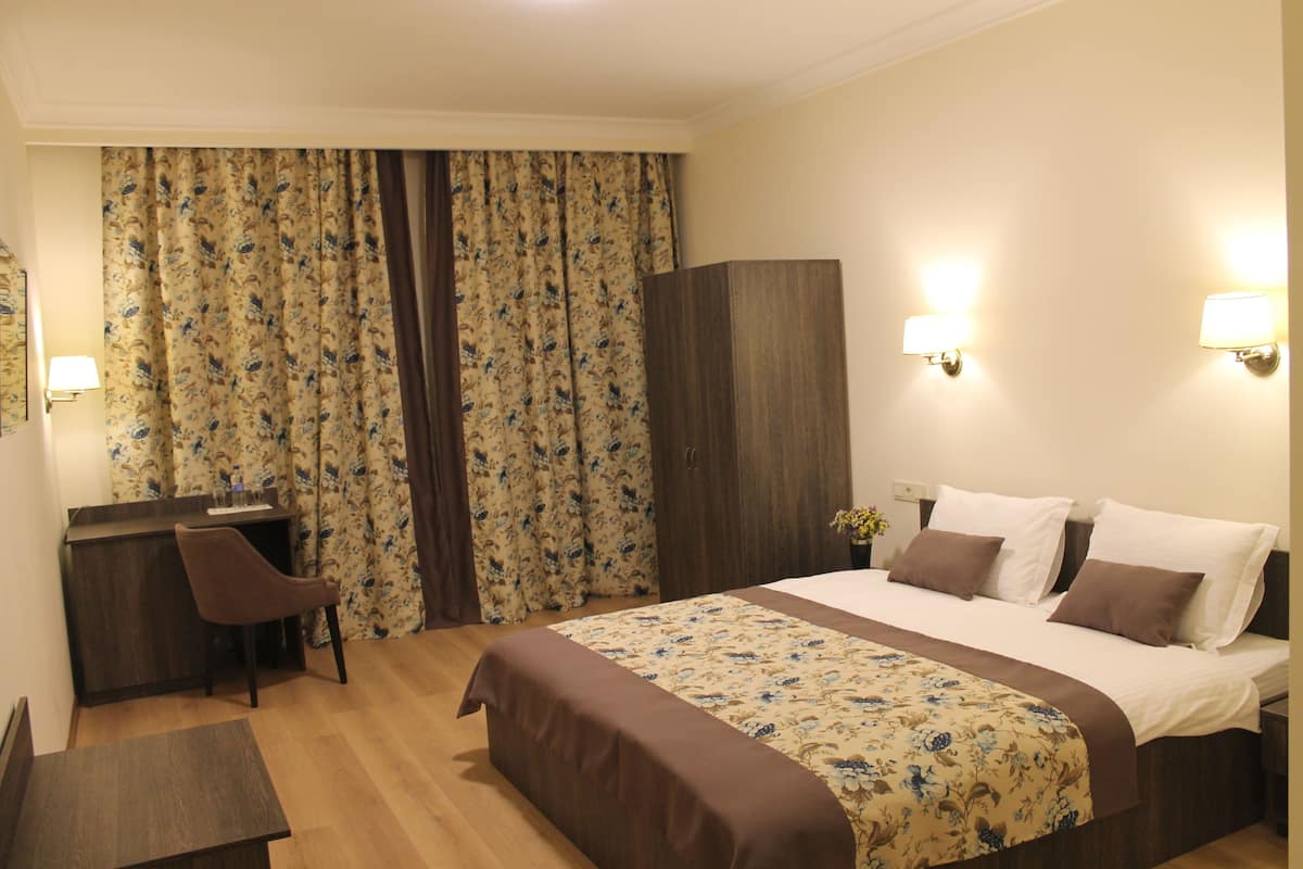 Ein Hotelzimmer mit Bett, Schreibtisch, Stuhl und Vorhängen.